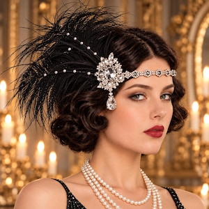 May include: A black feather headpiece featuring a silver-toned metal band adorned with clear crystals and small white pearls. The accessory includes a large, central crystal cluster with a dangling teardrop-shaped stone and a multi-strand pearl necklace.
