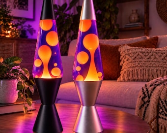 May include: Two lava lamps with conical bases and caps. The left lamp has a matte black base and cap, while the right lamp has a metallic silver finish. Both glass vessels contain a purple liquid with glowing orange wax blobs in motion.