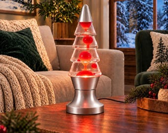 May include: A Christmas tree-shaped lava lamp with a silver metallic base and top. The clear glass vessel contains red wax blobs suspended in liquid, illuminated from the bottom by a light source, creating a glowing effect within the structure.