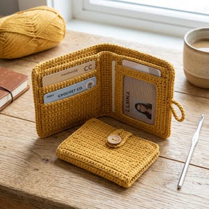 May include: A mustard yellow crocheted bifold wallet with a matching closed wallet featuring a wooden button closure. The open wallet displays multiple card slots, including one with the text "HANDMADE" and "CROCHET CO.", and a clear ID window.