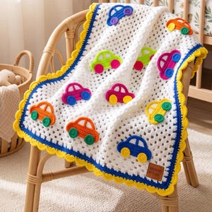 May include: A white crocheted baby blanket featuring a repeating pattern of small, colorful cars in shades of blue, orange, pink, yellow, and green. The blanket has a bright yellow scalloped border and a small brown rectangular tag at the corner.