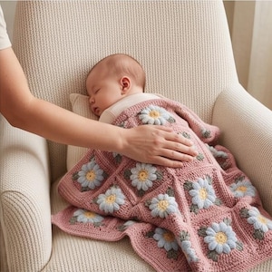 Op de afbeelding: Een gehaakte babydeken met een herhalend vierkant patroon met lichtblauwe en gele madeliefjesmotieven op een oudroze achtergrond. De deken ligt over een slapende baby en toont het gestructureerde haakwerk en het bloemmotief.