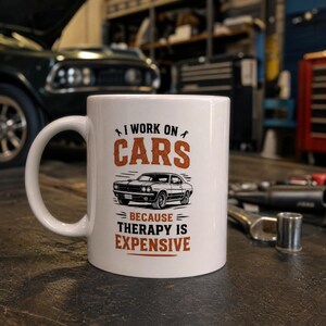 Puede incluir: Una taza de cerámica blanca con un gráfico en negro y naranja de un coche deportivo clásico. El texto dice: I WORK ON CARS BECAUSE THERAPY IS EXPENSIVE. El diseño incluye iconos de llaves inglesas sobre la palabra CARS y líneas horizontales.