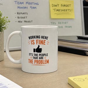 Może przedstawiać: Biały ceramiczny kubek z czarnym i pomarańczowym napisem Working Here Is Fine, It's The People That Are The Problem oraz czarną ikoną kciuka w górę. Kubek posiada standardowe ucho i gładki, cylindryczny korpus o klasycznym kształcie.