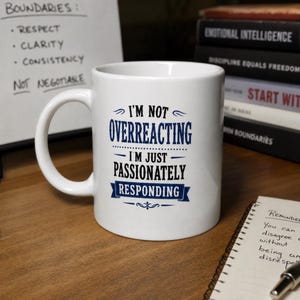Pode incluir: Uma caneca de cerâmica branca com o texto impresso em azul e preto I'M NOT OVERREACTING I'M JUST PASSIONATELY RESPONDING. A caneca tem um formato cilíndrico padrão com uma alça curva no lado esquerdo e um acabamento liso e brilhante.