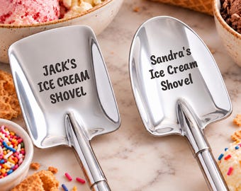 May include: Two polished stainless steel ice cream shovels with engraved text. The left shovel features the text JACK'S ICE CREAM SHOVEL, while the right shovel features the text Sandra's Ice Cream Shovel. Both have a spade-like head design.