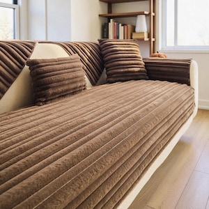May include: A brown sofa cover featuring a textured, ribbed, corduroy-like pattern. The set includes a long, rectangular piece covering the seat and backrest, along with a matching rectangular throw pillow, all in a solid, deep brown color.