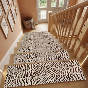 Peut inclure: Un ensemble de tapis d'escalier présentant un motif à rayures zébrées marron foncé et blanc. Les pièces rectangulaires sont installées sur des marches en bois, couvrant la partie centrale de chaque marche avec un motif animalier uniforme.