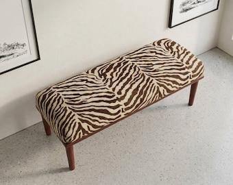 May include: A rectangular bench featuring a brown and cream zebra stripe pattern on the upholstered seat. The furniture piece is supported by four tapered wooden legs in a medium brown finish, providing a stable base for the padded top surface.