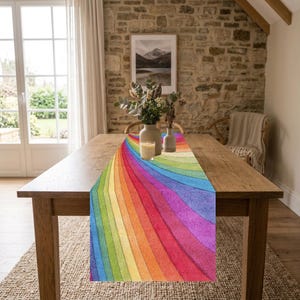 May include: A rectangular table runner featuring a vibrant, multi-colored rainbow pattern with curved, radiating stripes in shades of red, orange, yellow, green, blue, and purple, displayed flat on a wooden dining table surface.