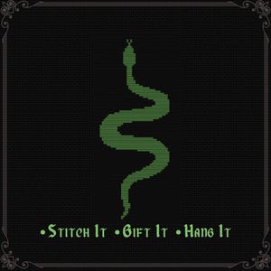 May include: A cross-stitch pattern featuring a green snake centered on a black grid background. Below the snake, the text reads "Stitch It • Gift It • Hang It" in a green gothic-style font. The entire design is enclosed in a decorative border.