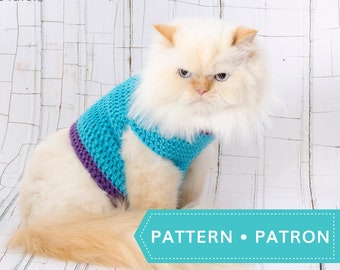 May include: A white long-haired cat wearing a blue and purple crocheted sweater. The cat is sitting on a white wooden surface. The text "PATTERN • PATRON" is visible in the lower right corner of the image.