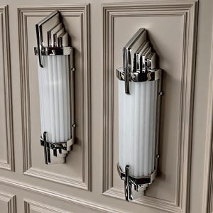May include: Two vertical wall sconces featuring polished chrome metal frames with stepped, geometric top and bottom accents. Each fixture contains a central cylindrical section composed of vertical, frosted white glass rods arranged in a parallel pattern.