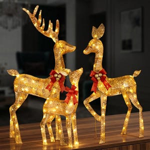 Könnte beinhalten: Ein Set aus drei beleuchteten Rentierfiguren aus goldfarbenem Netzmaterial. Jedes Rentier ist mit warmweißen LED-Lichtern am ganzen Körper ausgestattet und am Hals mit einer roten Stoffschleife verziert, die drei kleine goldene Kugeln trägt.