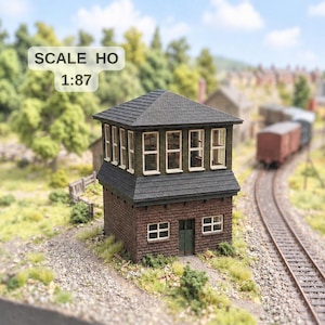 Può includere: Una cabina di segnalazione ferroviaria in miniatura in scala HO 1:87, con base in mattoni scuri, tetto in tegole scure e un livello superiore con molteplici finestre. La struttura presenta una piccola porta verde e infissi bianchi.