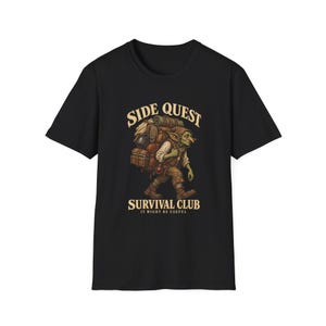 May include: A black t-shirt featuring a graphic of a green goblin carrying a large, heavy backpack filled with camping gear. The text above reads SIDE QUEST and below reads SURVIVAL CLUB IT MIGHT BE USEFUL in a light beige, vintage-style font.