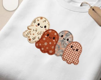 May include: A white crewneck sweatshirt featuring an embroidered design of four small ghosts. The ghosts have different patterns: one with floral prints, one with white snowflakes on orange, one with a gray marble effect, and one with brown gingham.