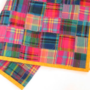 May include: A patchwork quilt with a yellow border. The quilt is made of squares of plaid fabric in shades of pink, blue, green, and purple.