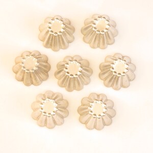 May include: Seven silver-colored metal molds for baking individual desserts. The molds are shaped like flowers with fluted edges and a smooth, round center.