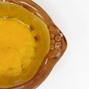 May include: A yellow ceramic bowl with a brown rim and a floral design. The bowl is empty and has a glossy finish.