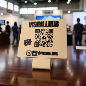 Puede incluir: Un letrero cuadrado de color beige con letras negras en relieve que dicen VISIBILLHUB, un código QR central con un logotipo VH, un pequeño icono de burbuja de texto que dice SCAN ME e iconos de redes sociales Instagram y LinkedIn.