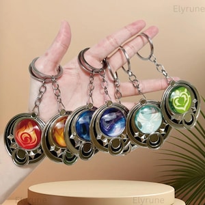 May include: A set of six circular metal keychains featuring colorful, glossy, domed inserts with distinct elemental symbols. Each keychain has a silver-toned frame with decorative geometric cutouts and a sturdy split ring attached by a chain.