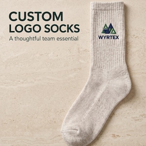 Puede incluir: Un calcetín de color beige claro con textura acanalada que presenta un logotipo triangular verde y azul sobre el texto WYRTEX. La imagen incluye el texto CUSTOM LOGO SOCKS A thoughtful team essential en letras verde oscuro.