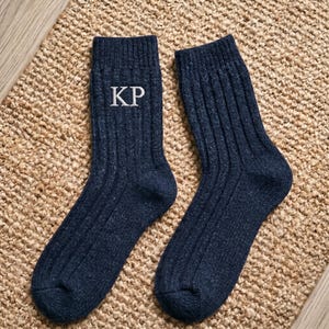 Puede incluir: Un par de calcetines de punto acanalado en color azul marino oscuro con las letras blancas bordadas KP en el puño superior de uno de los calcetines. Los calcetines tienen una apariencia texturizada y jaspeada con un diseño clásico.