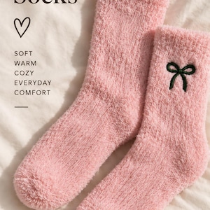 Puede incluir: Un par de calcetines rosas suaves y peludos con un lazo bordado en verde oscuro en el lateral. El texto dice: Fuzzy Socks, SOFT WARM COZY EVERYDAY COMFORT y Little Details Brighter Days, junto a un s&iacute;mbolo de coraz&oacute;n y una l&iacute;nea.