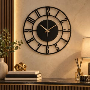 May include: A round wall clock featuring a black open-frame design with large cut-out numerals. The centre consists of a solid black circular dial with thin gold-toned hour, minute, and second hands, creating a high-contrast look for the wall.
