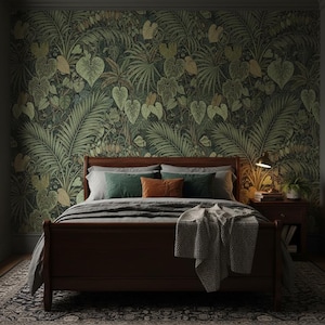 May include: A dark wood bed frame with a gray duvet and a textured throw blanket. The bed features two dark green pillows and one burnt orange pillow. The wall behind the bed is covered in wallpaper with a dense pattern of green tropical leaves.