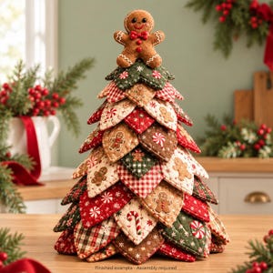 May include: A decorative fabric Christmas tree constructed from layered, quilted leaf-shaped patches in red, green, and cream with gingerbread man and candy cane patterns, topped with a plush gingerbread man figure. Text reads: Finished example Assembly required.