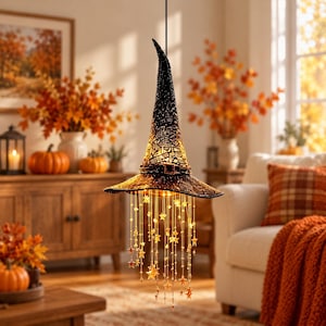 May include: A black witch hat pendant light featuring a textured, lace-like surface and a decorative band. The hat is illuminated from within, and numerous thin, dangling gold chains adorned with small star-shaped charms hang from the brim.