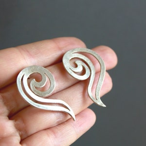 May include: A pair of silver earrings with a swirling, abstract design. The earrings are shaped like a teardrop with a spiral detail.