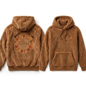 以下が含まれることがあります： ドローストリング付きフードとカンガルーポケットを備えた、茶色のふわふわしたフリースパーカー。背面には「Thankful」という文字を囲むカラフルな秋の葉の刺繍リースがあり、前面には小さな葉のエンブレムがあしらわれています。