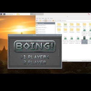 May include: A computer screen displaying a game called "BOING!" with the options "1 PLAYER" and "2 PLAYER". The game is set against a background of a sunset over a landscape.