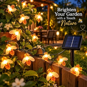 Puede incluir: Una guirnalda de luces LED con forma de abeja, alas translúcidas y cuerpos de color ámbar brillante, colocada sobre una valla de madera. Un panel solar negro sobre una estaca está conectado a las luces. Texto: Brighten Your Garden with a Touch of Nature.