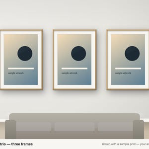 May include: A set of three rectangular picture frames with light wood borders. Each frame contains a print featuring a dark blue circle, a horizontal white line, and the text "sample artwork" on a blue and beige gradient background.