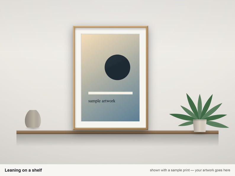 May include: A rectangular wooden picture frame containing a print with a gradient background, a dark blue circle, a horizontal white line, and the text "sample artwork" in black, positioned on a shelf next to a small vase and a plant.