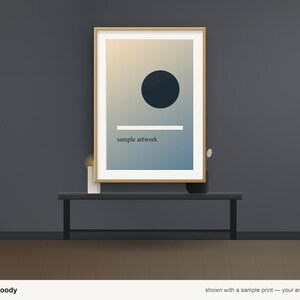 May include: A rectangular wooden frame containing a print with a gradient background, a dark circle, a horizontal white line, and the text "sample artwork" in a small, dark, sans-serif font, centered on a dark gray wall.