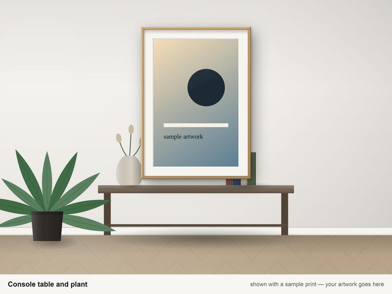 May include: A rectangular wooden frame containing a print with a gradient background, a dark circle, a horizontal white line, and the text "sample artwork". The frame sits on a dark brown console table next to a vase and a green plant.