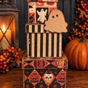 May include: A stack of three square decorative boxes with Halloween themes. The top box features cats, ghosts, and the text Trick or TREAT. The middle box has black and white vertical stripes. The bottom box displays a diamond pattern with skulls and pumpkins.
