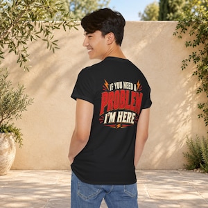 May include: A black short-sleeved t-shirt featuring a graphic on the back with the text IF YOU NEED A PROBLEM I'M HERE in red and cream lettering, accented by orange lightning bolt symbols and decorative lines on a dark background.