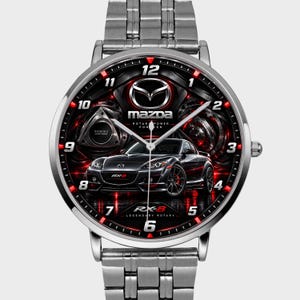 Pode incluir: Um relógio de pulso analógico prateado com pulseira de elos metálicos. O mostrador apresenta um fundo preto com um gráfico de um carro Mazda RX-8, o logótipo da Mazda e o texto "RX-8 LEGENDARY ROTARY" e "ROTARY POWER FOREVER" em branco e vermelho.