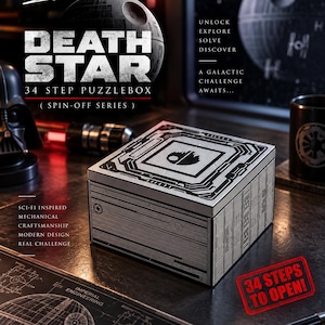 May include: A square mechanical puzzle box featuring a silver and black design with intricate paneling and a Death Star emblem on the lid. The box is labeled Death Star 34 Step Puzzlebox, with text including Unlock Explore Solve Discover and 34 Steps To Open.