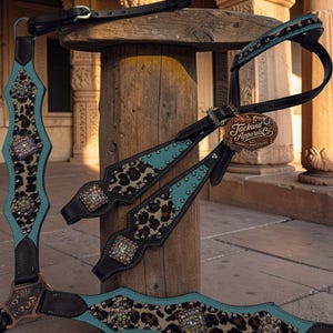 May include: A dark brown leather horse breast collar and headstall set featuring turquoise leather overlays, leopard print patterns, and square crystal conchos. The set includes silver-tone metal studs and a brown tag reading Jackand Apparels Co.