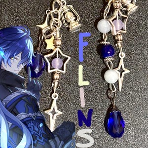 May include: A phone charm and a dangling accessory featuring silver-toned metal star charms, miniature lantern charms, and blue and white beads. The set includes a character illustration with blue hair and the vertical text FLINS.