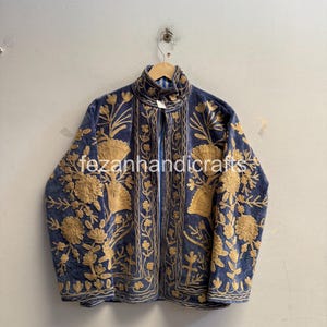 May include: A blue jacket featuring intricate gold-colored floral embroidery throughout the front and sleeves. The garment has a high collar and a vertical opening down the center. The text "fezanhandicrafts" is visible across the middle.