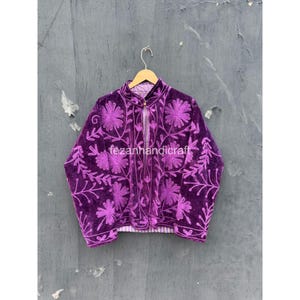 Puede incluir: Una chaqueta de terciopelo morado oscuro con intrincados bordados florales en un tono morado más claro. La chaqueta tiene cuello mao, mangas largas y una abertura frontal con un solo botón. El texto fezanhandicraft es visible.