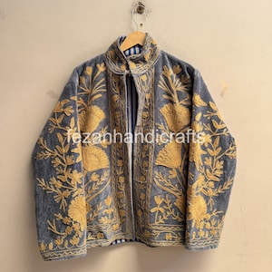 Pode incluir: Uma jaqueta cinza com intrincados bordados florais dourados na frente e nas mangas. A peça possui gola alta, mangas compridas e um forro listrado azul e branco visível. O texto fezanhandicrafts está impresso na parte da frente.